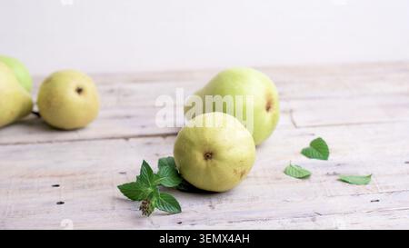 A minimalist high angle shot displays ripe green pears arranged on a weathered light wooden table alongside fresh mint leaves with a clean white backg Stock Photo