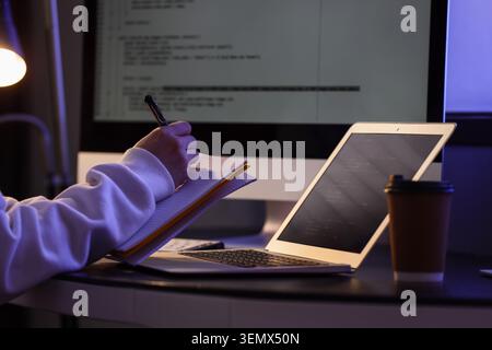 Female programmer's hands writing on notebook in dark office at night Stock Photo