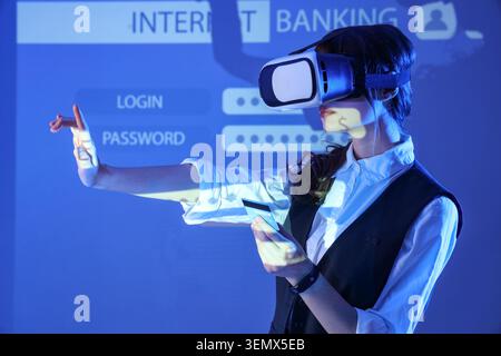 Young businesswoman in VR glasses with credit card using virtual screen against interface of web application. Online banking concept Stock Photo