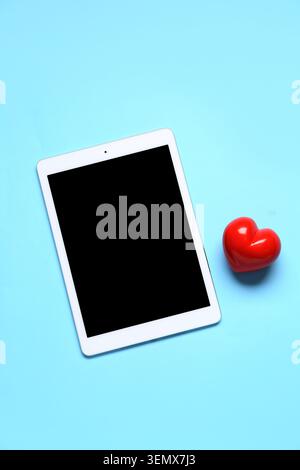 Tablet computer with red heart on blue background. Concept of online dating Stock Photo