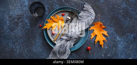 Autumnal table setting with golden oak leaves, berries, and cutlery on dark textured background for seasonal dining Stock Photo