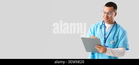 Smiling male doctor in scrubs with stethoscope writing on clipboard, medical professional healthcare worker Stock Photo