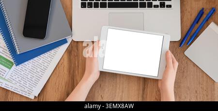 Overhead view of hands holding tablet with blank screen on wooden desk with laptop and office supplies, hands hold a tablet with a blank white screen, Stock Photo