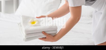 Hotel housekeeping staff placing freshly folded white towels with plumeria flower on clean bedding Stock Photo