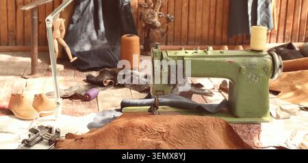 Vintage green sewing machine with leather pieces and thread spools on a wooden floor, craftsmanship and handmade production Stock Photo