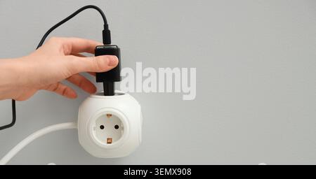Hand plugging black charger into white multi-socket power strip for device charging and electrical connection, this action represents device charging, Stock Photo