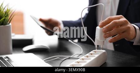 Businessman plugging charger into power strip for tablet, energy consumption and technology integration in modern office Stock Photo