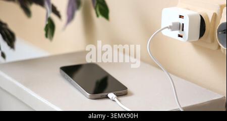 Modern smartphone charging with multi-port USB adapter plugged into wall outlet, digital device power supply, the digital device receives power throug Stock Photo