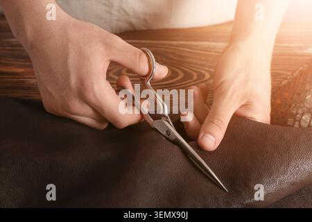 Craftsman hands cutting brown leather with scissors, handmade goods production, tailoring and repair workshop Stock Photo