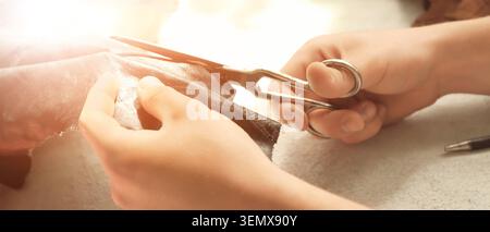 Craftsman hands cutting leather with scissors, tailoring and fashion design process, handmade goods production Stock Photo