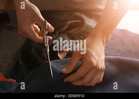 Craftsperson cutting leather with scissors handmade goods production artisan workshop textile manufacturing creative hobby Stock Photo
