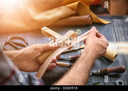 Artisan crafting leather belt with hand tools traditional leatherwork process handmade goods production small business workshop Stock Photo