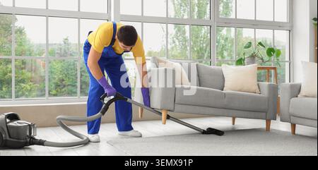 Professional cleaning service worker vacuuming living room carpet for home maintenance and hygiene, the modern interior with a sofa and large window p Stock Photo