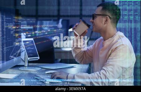 Young male developer drinking coffee while coding on computer, software development and data analysis Stock Photo