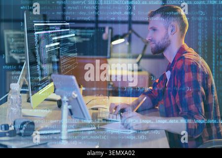 Young male programmer coding software on computer screen with data overlay, digital technology and development Stock Photo