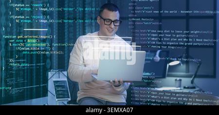 Smiling male programmer working on laptop with overlayed code, software development and digital technology Stock Photo