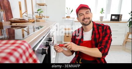 Professional appliance repairman fixing kitchen oven with screwdriver, home maintenance and technical service Stock Photo