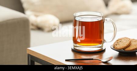 Relaxing afternoon tea break with hot beverage and cookies on a modern wooden table in a cozy living room, two chocolate chip cookies are on a small b Stock Photo