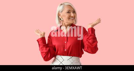 Smiling senior woman presenting with open hands, confident mature lady gesturing to side, isolated on pink background Stock Photo