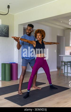 African American woman African man in sportswear practicing yoga at home guiding arms on black mats Stock Photo