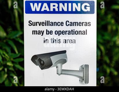 Warning sign for surveillance cameras in operation on green foliage background, Auckland New Zealand Stock Photo