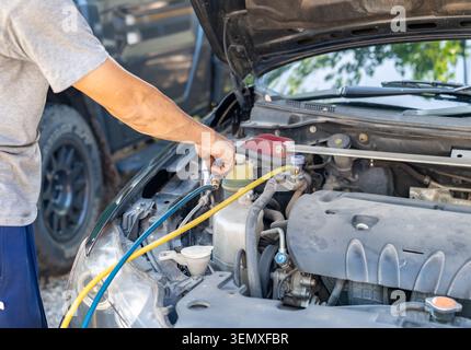 Close-up of a technician servicing a vehicle's AC system, checking pressure with blue and yellow hoses during routine automotive maintenance. Stock Photo