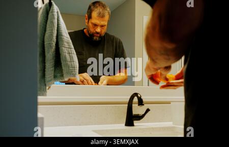 Middle aged man taking daily vitamins prescription medicine pills bathroom mirror routine healthy aging healthcare compliance self care grooming Stock Photo