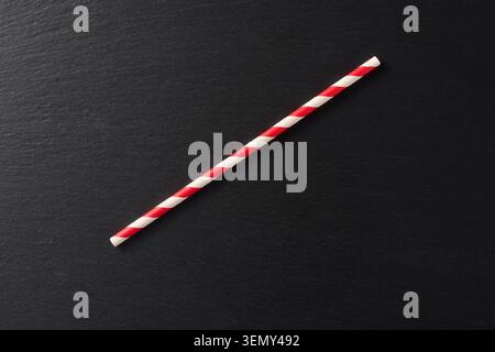 red and white striped paper straw on dark slate stone, eco friendly drinking utensil with retro pattern, top view with copy space Stock Photo