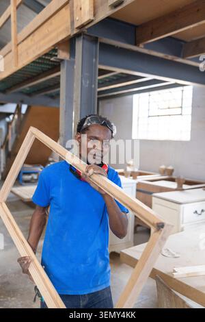African American man holding rectangular frame at woodshop, wearing hearing protection and goggles Stock Photo