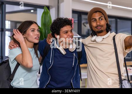 Diverse teenage students smiling and posing on campus with backpacks headphones and beanie on right. Trio, friends, classmates, coworking, lounge, int Stock Photo