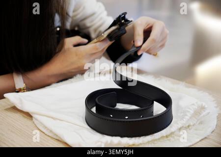 Woman using a magnifying glass to check the authenticity of a leather belt Stock Photo
