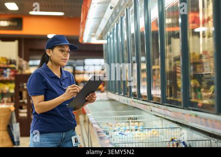 Hispanic Woman Working in Supermarket and Checking Frozen Inventory Stock Photo
