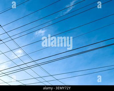 A clear blue sky is filled with many power lines. The lines run in different directions. Some clouds are visible in the background. It is daytime and Stock Photo