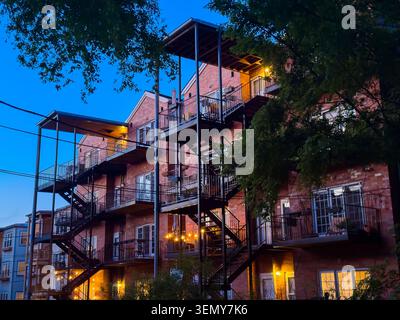 Groups of people sit and stand on balconies of an apartment building at night with warm lights shining. The blue sky shows that evening has arrived. Stock Photo