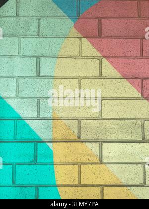 Bright colored shapes cover a brick wall in a modern setting. The mural features blue, yellow, pink, and off-white colors arranged in a geometric desi Stock Photo