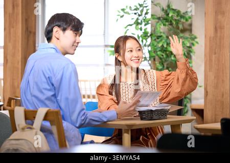Japanese young male and female students smiling talking and calling for service at a cafe Stock Photo