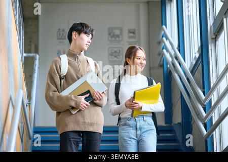 Japanese male and female university students smiling and walking down campus stairs with laptops Stock Photo