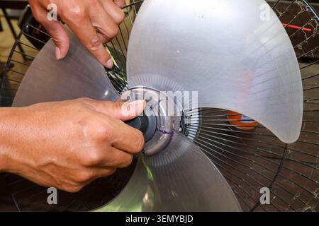 Focused hand performs careful electric fan repair, fixing plastic blade during routine maintenance and cleaning, showing patient dedication to househo Stock Photo