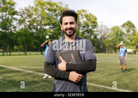 Arab Soccer Coach Smiling On Outdoor Football Field With Players Stock Photo