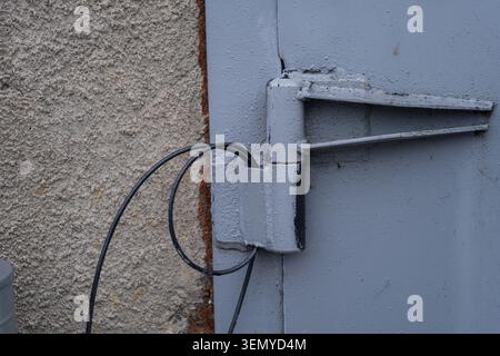 Close up of a heavy duty industrial metal door hinge with connected wiring on a utility or service entrance. Infrastructure detail representing indust Stock Photo
