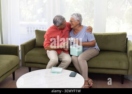 Senior couple sitting on olive-green sofa in living room holding light-blue box and B and W scan Stock Photo
