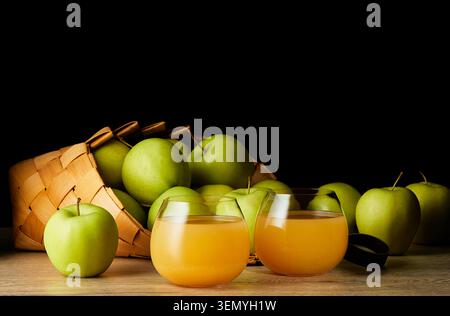 Fresh apple juice served in two glasses with ripe green apples in wicker basket on wooden table against black background. Healthy organic drink. Stock Photo