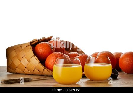 Two glasses of fresh orange juice with ripe oranges in wicker basket isolated on white background. Healthy citrus beverage with copy space. Stock Photo