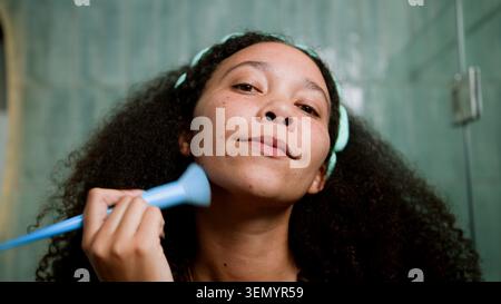 Black Woman Applying Makeup in Bathroom Mirror During Morning Self-Care Routine Stock Photo