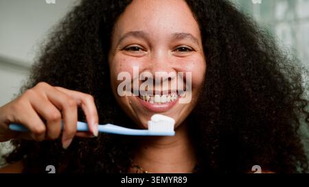 Smiling Woman Brushing Teeth With Toothbrush During Morning Oral Hygiene Routine In Bathroom Stock Photo