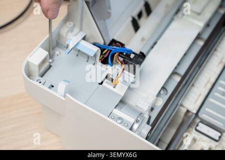 Hand using a screwdriver to repair an inkjet printer interior, revealing cables, connectors and mechanical components during routine maintenance and t Stock Photo