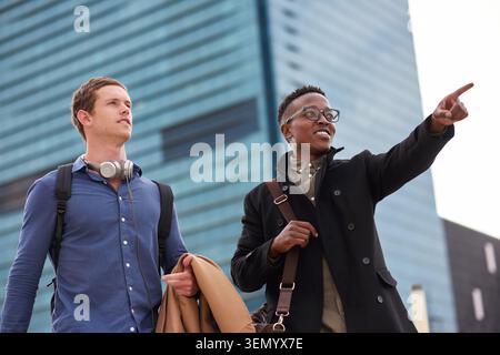 Commute, friends and business people with pointing in city, morning bonding and direction to work. Travel, coworkers and happy men with discussion in Stock Photo