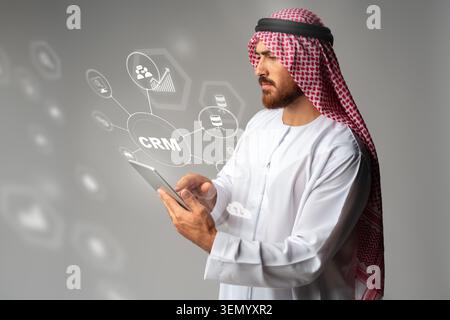 Man in traditional attire using tablet to manage CRM data and tools for customer connection Stock Photo