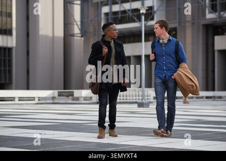 Walking, friends or business people with conversation in city, investment idea or bonding on commute. Morning travel, coworkers or men with Stock Photo