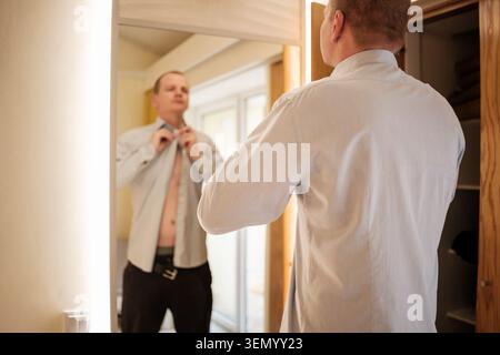 Man getting dressed in front of a mirror, preparing for his day Stock Photo